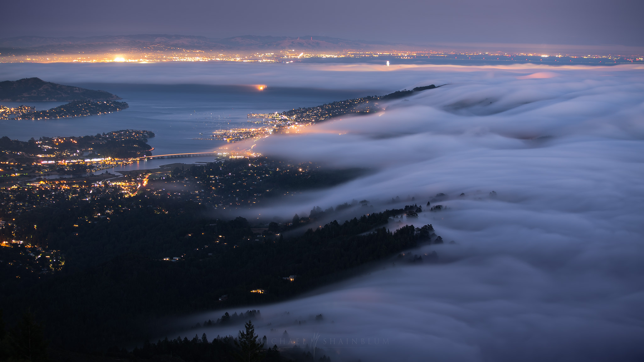 Rolling fog over San Francisco Bay at night, city lights glowing underneath